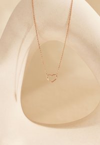 Roze gouden hartketting op een delicate ketting, weergegeven tegen een neutrale, textuur achtergrond met zachte rondingen.