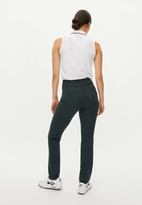 Pantaloni aderenti verde scuro realizzati in materiale elasticizzato, con vita alta e tasche posteriori, abbinati a una maglietta bianca senza maniche e sneakers bianche.