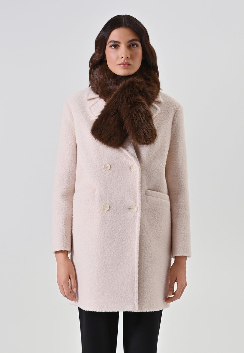 Manteau en laine rose clair à double boutonnage avec deux poches avant et boutons crème, associé à une écharpe en fausse fourrure marron foncé.