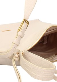 Borsa a mano in pelle beige chiaro con finitura texturizzata, zip dorata e tracolla. L'interno è foderato in un morbido tessuto beige.