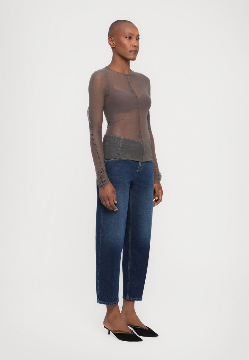 Langærmet, gennemsigtig brun bluse med knaplukning, parret med mellemhøje, løstsiddende mørkeblå jeans og sorte spidse hæle.