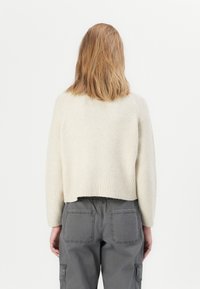 Maglione a maglia crema tagliato con orlo a coste, con maniche testurizzate. Abbinato a pantaloni cargo grigi con tasche posteriori.