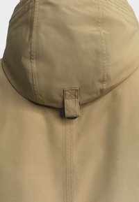 Béžová kapucňová bunda s hladkým povrchom, ktorá sa zapína na gombíky a má posilnené stehy pozdĺž švov.