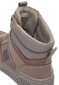 Pruun välisaap, millel on tekstureeritud naha- ja lõuendipealne, polsterdatud krae ning tugev kummisest tald. Omab külgmist logo ja tugevdatud õmblusi.