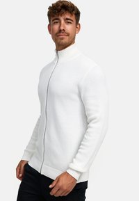 Sudadera blanca con cremallera, con un diseño de punto texturizado y puños de canalé. Presenta un cuello alto y una silueta ceñida y elegante.
