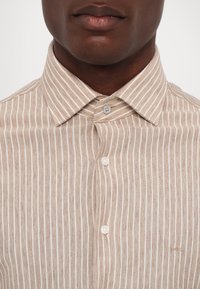 Gros plan d'une personne portant une chemise à rayures verticales beige et blanche avec un col classique, montrant uniquement les lèvres et le menton.
