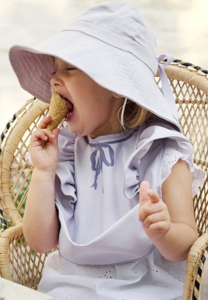 Bambino con una bavetta di pizzo lavanda e cappello di paglia, che si gode un cono di gelato. L'ambientazione presenta una sedia intrecciata e toni morbidi e neutri.