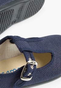 Zapato de tela azul marino con una textura tejida transpirable, diseño de punta cerrada, cortes laterales y un acento de hebilla plateada. Suela plana de goma.