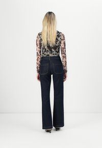 Jean taille haute bleu foncé avec une jambe évasée, associés à un haut transparent à manches longues avec un motif léopard.