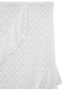 Tissu en dentelle blanche avec un motif floral, présentant une texture douce et un design fluide, tombant élégamment avec des bords froncés.