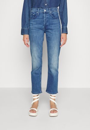 Dolna część ciała ubrana w niebieskie, wysokie w talii, proste spodnie dżinsowe z wyblakłymi udami oraz białe sandały na platformie z paskami wokół kostki.