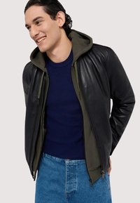 Svart läderjacka med en olivgrön huva, dragkedja framtill och ribbade ärmslut. Bärs över en marinblå tröja och jeans i denim.