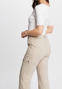 Biały prążkowany top z krótkim rękawem w zestawieniu z beżowymi, wysokim stanem spodniami cargo z bocznymi kieszeniami i złotymi guzikami.