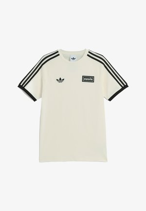 Biała koszulka Adidas z czarnymi paskami na rękawach, czarnymi mankietami, logo Adidas po lewej stronie klatki piersiowej oraz naszywką "oasis" po prawej stronie klatki piersiowej.