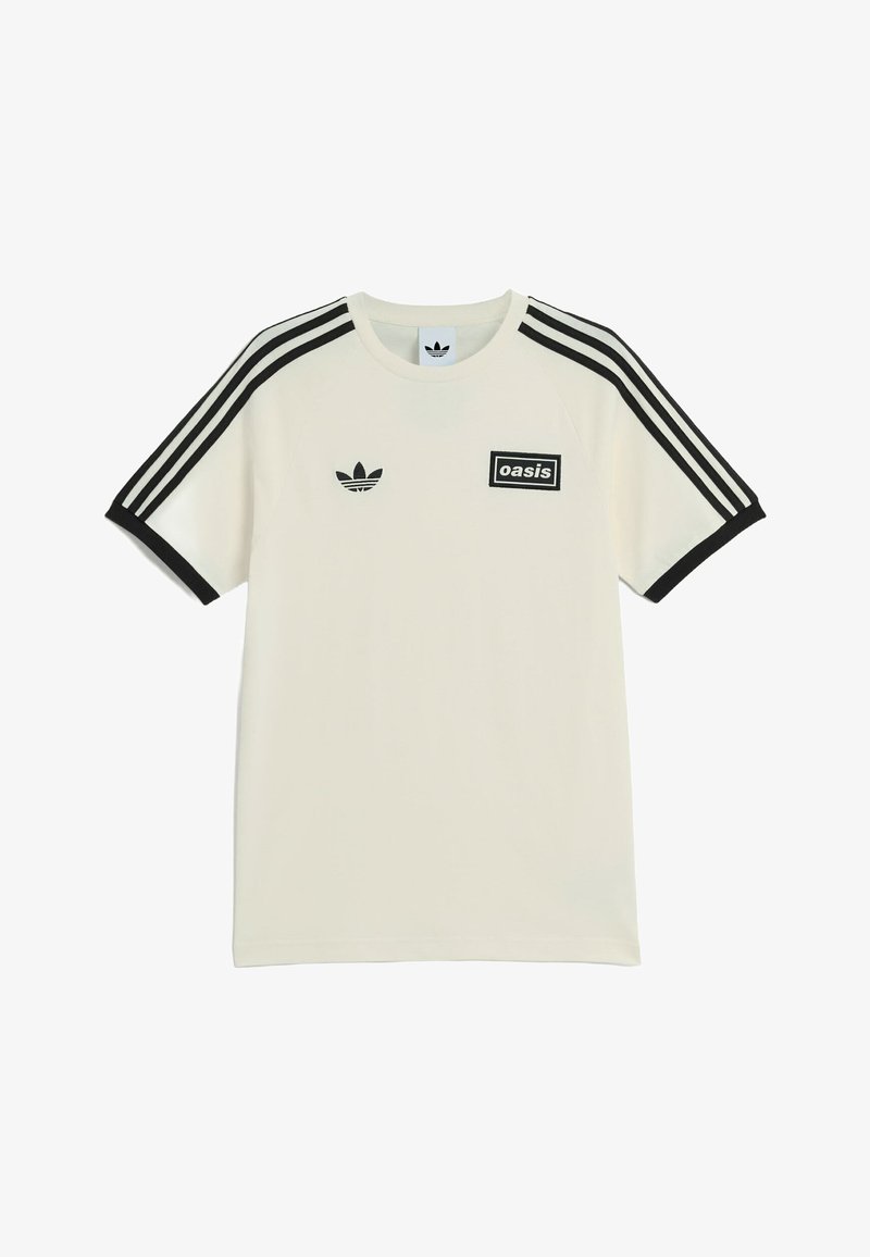 Maglietta bianca Adidas con strisce nere sulle maniche, polsini neri, logo Adidas sul lato sinistro del petto e patch "oasis" sul lato destro del petto.