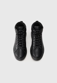 Zapatillas negras de caña alta hechas de cuero suave, con cordones planos, ojales de metal y una suela de goma texturizada.