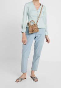 Ljusblå blus med knappar, kombinerad med högmidjade ljusa denimjeans och sandaler med öppen tå i ormtryck. Liten handväska i ormtryck.