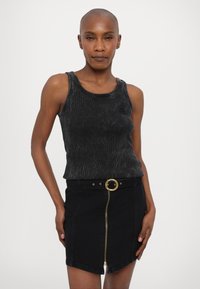 Svart ribbestrikket tank topp med rund hals, kombinert med et svart denimskjørt med frontglidelås og et belte med gullfarget, sirkulært spenne.