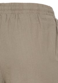 Pantalon beige avec taille élastique, texture de tissu douce et détails de couture subtils autour de la taille.