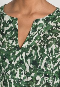 Gros plan d'un col avec un col cranté sur un tissu blanc recouvert d'un imprimé botanique à feuilles vertes.