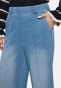 Pantalon en denim bleu clair à jambes larges avec une texture lisse, doté de poches latérales et de détails de couture centrés.