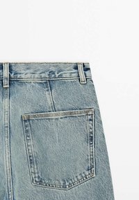 Vue arrière d'un jean en denim bleu clair présentant une seule grande poche arrière et des passants de ceinture doubles sur fond blanc.