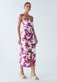 Robe imprimée fleurie en crème et violet, avec un décolleté carré, des fines bretelles et une fente à l'avant, confectionnée en tissu léger.