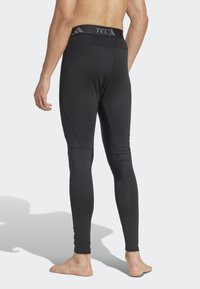 Leggings atletici neri con un motivo testurizzato sulla parte inferiore delle gambe e una vita alta con logo. Il materiale sembra elastico e aderente.