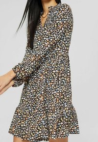 Robe florale noire avec une jupe à volants, des manches longues et un décolleté en V. Le tissu présente de petites fleurs colorées dans des nuances de bleu, pêche et jaune.