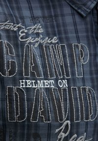 Blau kariertes Hemd mit weißen und grauen gestickten Text. Der Text enthält "CAMP DAVID" und "HELMET ON" sowie ein strukturiertes Stickdetail.