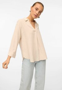 Chemise col rose clair avec un col en V, des manches trois-quarts et un ourlet droit, fabriquée dans un tissu doux et texturé.