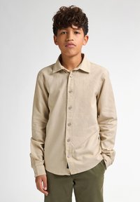 Beige overhemd met lange mouwen en knoopsluiting, voorzien van een kraag, met een gladde textuur en knoopsluiting aan de voorkant, gecombineerd met olijfgroene broek.