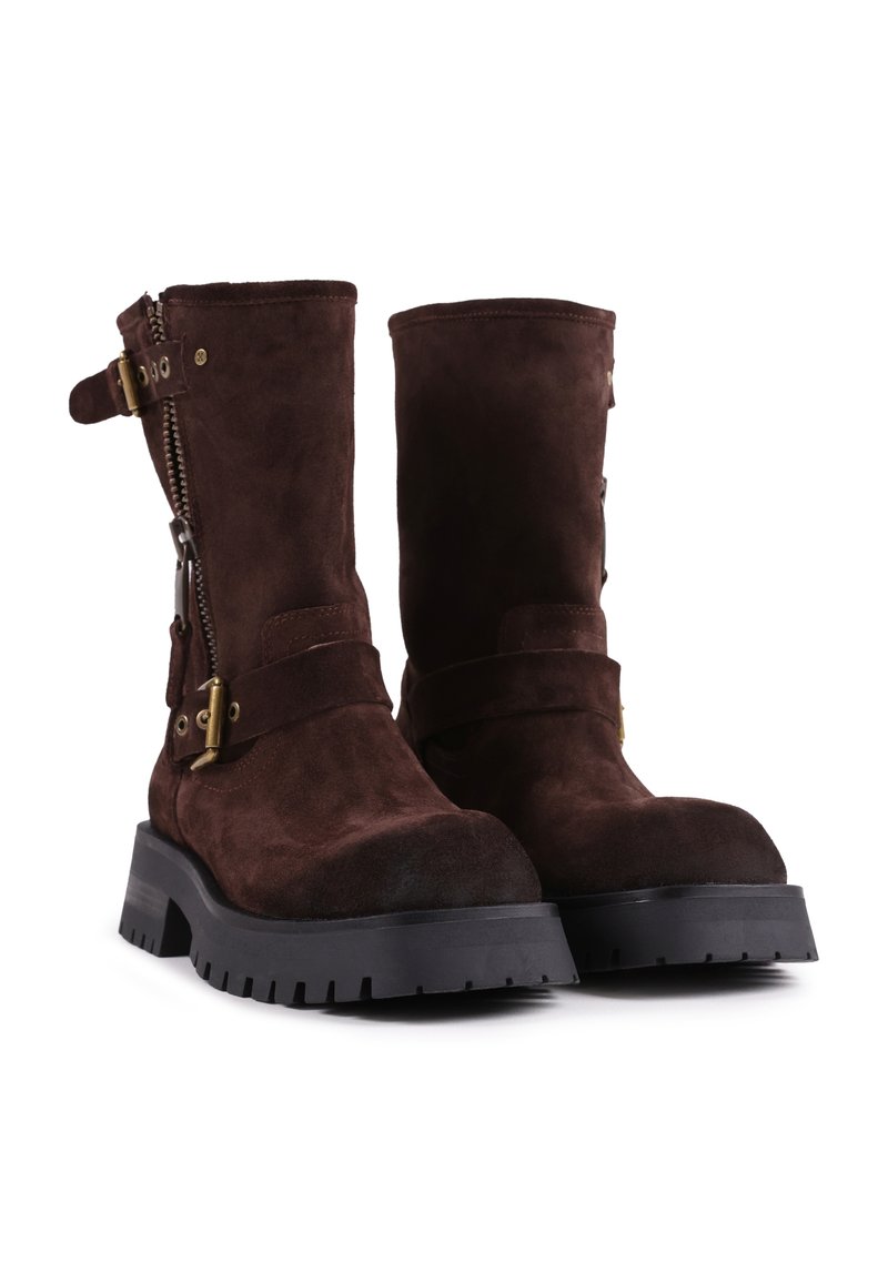 Braune Wildleder-Stiefeletten mit runder Zehenpartie, seitlichem Reißverschluss und metallischen Riemenakzenten. Obermaterial aus strukturiertem Leder und rutschfester schwarzer Gummisohle.