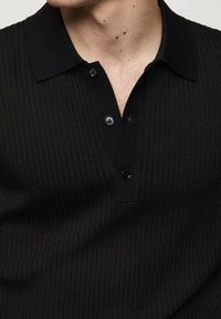 Černé žebrované polo tričko s límečkem, se třemi černými knoflíky a texturovanou tkaninou. Detailní záběr, který zdůrazňuje detaily.