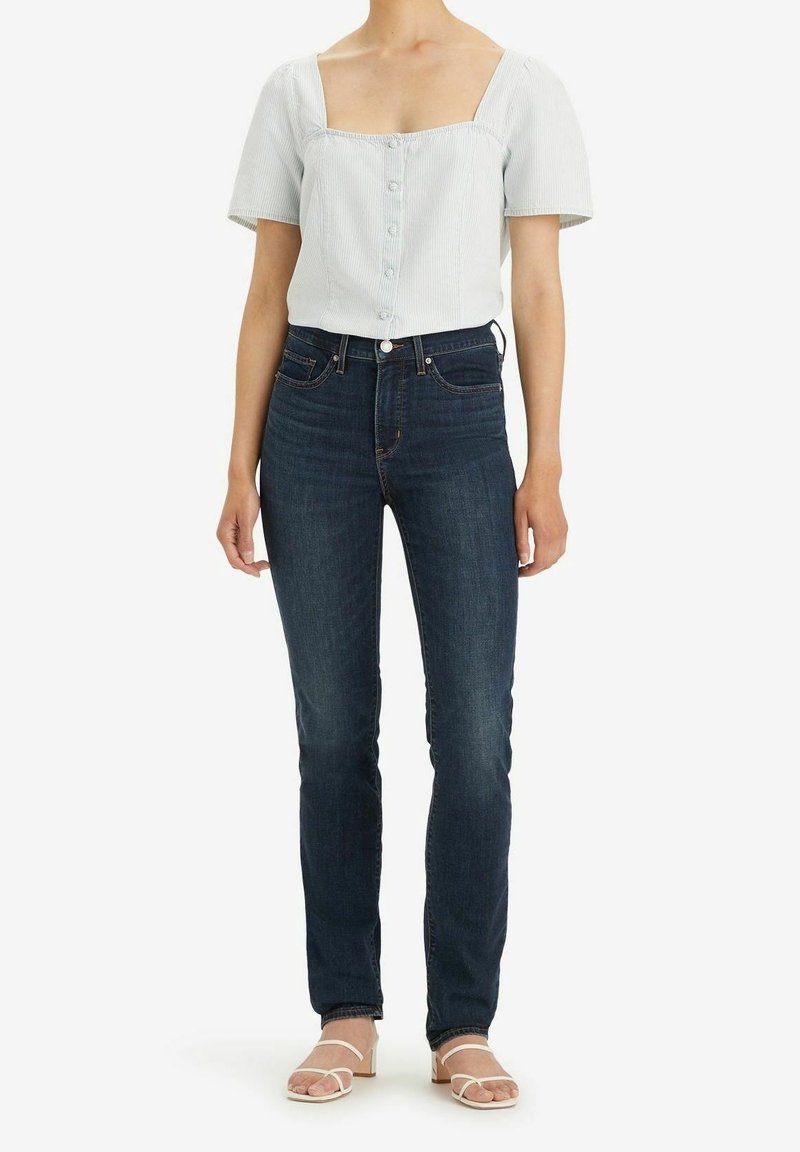 Ljusblå skjorta med fyrkantig halsringning och korta puffärmar, parat med mörkblå slim-fit jeans och vita sandaler med remmar.