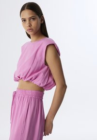 Top corto rosa con mangas cortas enrolladas y cintura fruncida. Combinado con pantalones rosa de cintura elástica con cordón a juego.