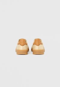 Leather sneakers with a two-tone design: tan leather heel and cream body. Textured rubber sole, rounded shape, minimalistic detailing.