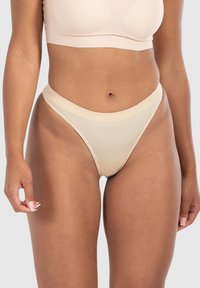 Beige nahtloser Tanga-Unterwäsche mit einer glatten, dehnbaren Textur und einem dünnen Bund, entworfen für minimale Sichtbarkeit unter der Kleidung.