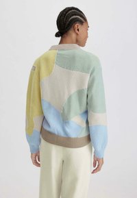 Neulottu villapaita pastelliväreissä, jossa on abstrakteja kuvioita keltaisessa, vihreässä, sinisessä ja beessissä. Ribatut hihansuut ja helma, rento malli.