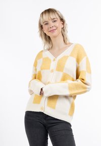 Sárga és krémszínű kockás kardigán hosszú ujjakkal, V kivágással és gombos záródással. Puha kötött textúra, oversized fazon.