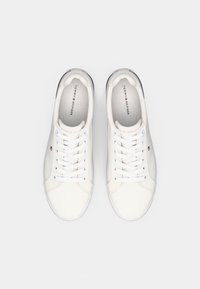 Une paire de baskets blanches Tommy Hilfiger avec des lacets blancs, vue de dessus sur un fond blanc uni.