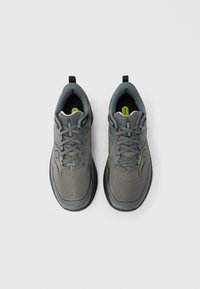 Zapatillas deportivas de malla gris con superficie texturizada, suela negra y plantilla verde. Cuentan con una lengüeta para tirar y punta reforzada.