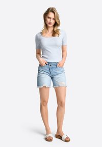 Gestreiftes Kurzarmoberteil in Blau und Weiß, kombiniert mit hellen Jeansshorts mit ausgefranstem Saum und zerrissenen Details, getragen mit weißen Riemchensandalen.