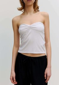 Witte geribbelde strapless top met een gedraaide voorkant, gecombineerd met zwarte broek met touwtjes, die een fitted ontwerp en cropped lengte toont.