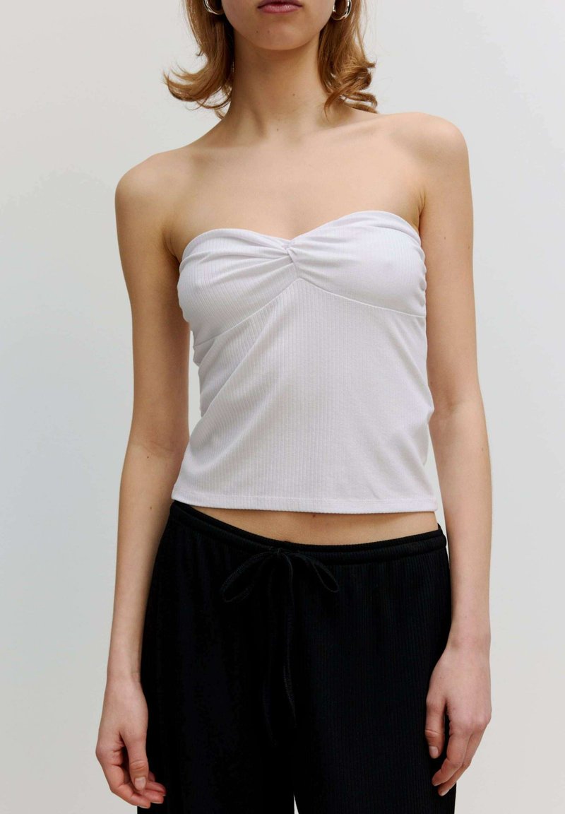 Witte geribbelde strapless top met een gedraaide voorkant, gecombineerd met zwarte broek met touwtjes, die een fitted ontwerp en cropped lengte toont.