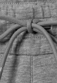 Gros plan sur une ceinture en tissu gris avec un cordon gris noué comportant des embouts métalliques.