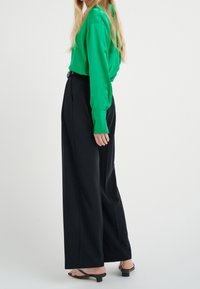 Blusa di seta verde e pantaloni neri a gamba larga a vita alta. La blusa ha maniche lunghe e una texture liscia; i pantaloni presentano un taglio pulito.