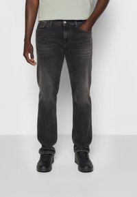 Jeans de mezclilla negra con corte recto, detalles de desgaste ligero, cinco bolsillos y cierre de botón plateado. Combinados con zapatillas negras.