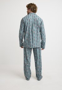 Men's pajama set in light blue fabric, featuring nutcracker print. Loose-fitting shirt with collar and long sleeves, paired with matching pants.