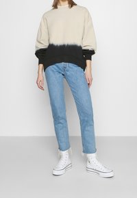 Sweat-shirt beige et noir dip-dye avec épaules tombantes, associé à un jean droit bleu clair et des baskets montantes blanches.